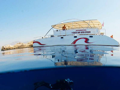 Man diving under a day pontoon catamaran sailing near Grebeni islands in Dubrovnik